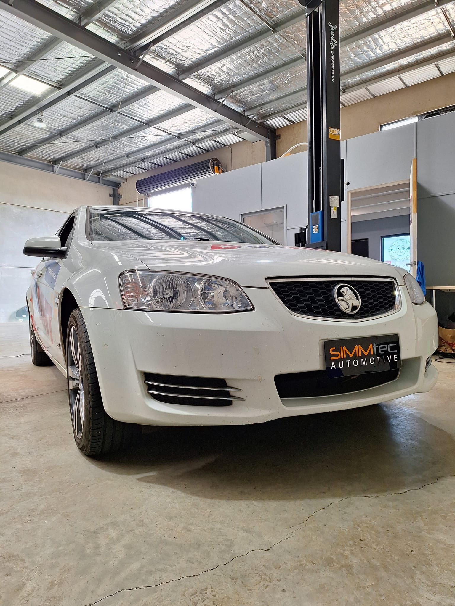 A white car is parked in a garage on a lift.