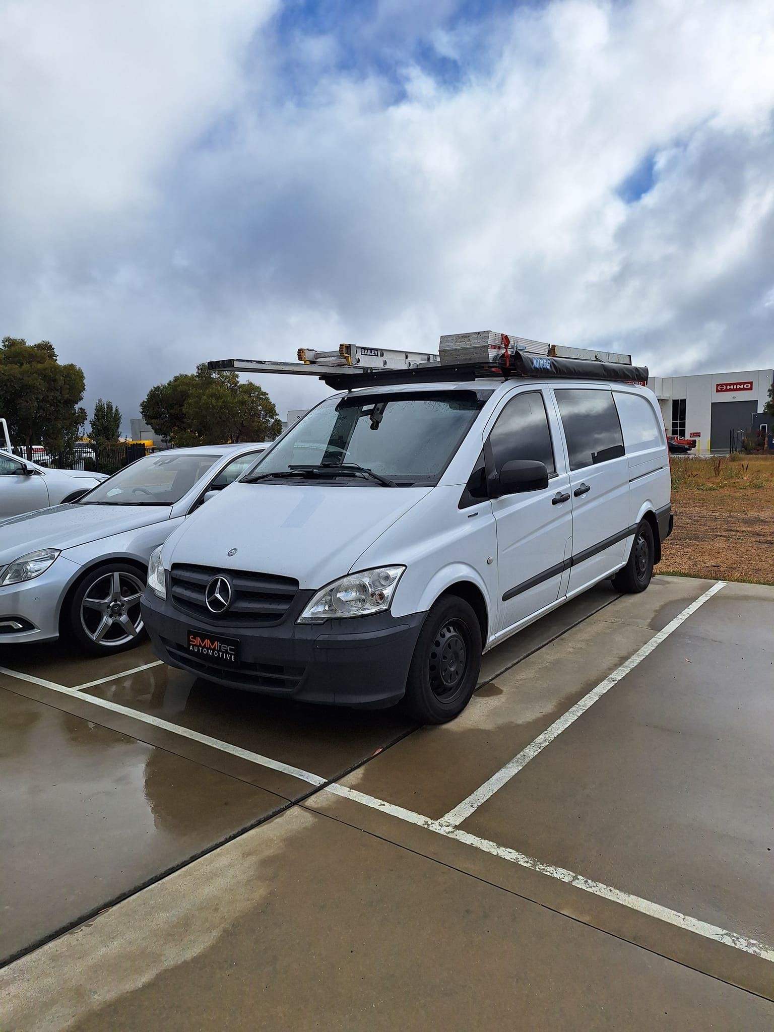 A white van with a roof rack is parked in a parking lot.