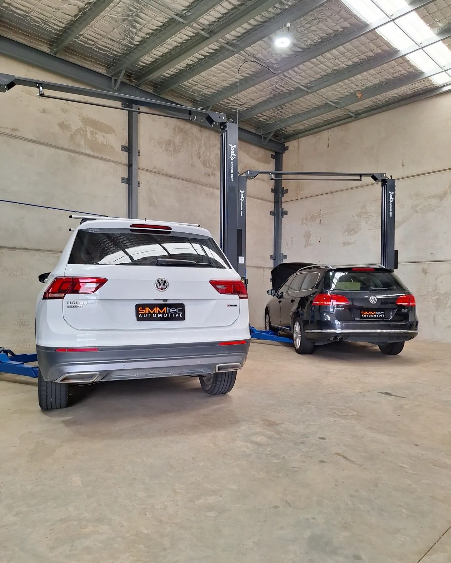 Two cars are parked in a garage on a lift.
