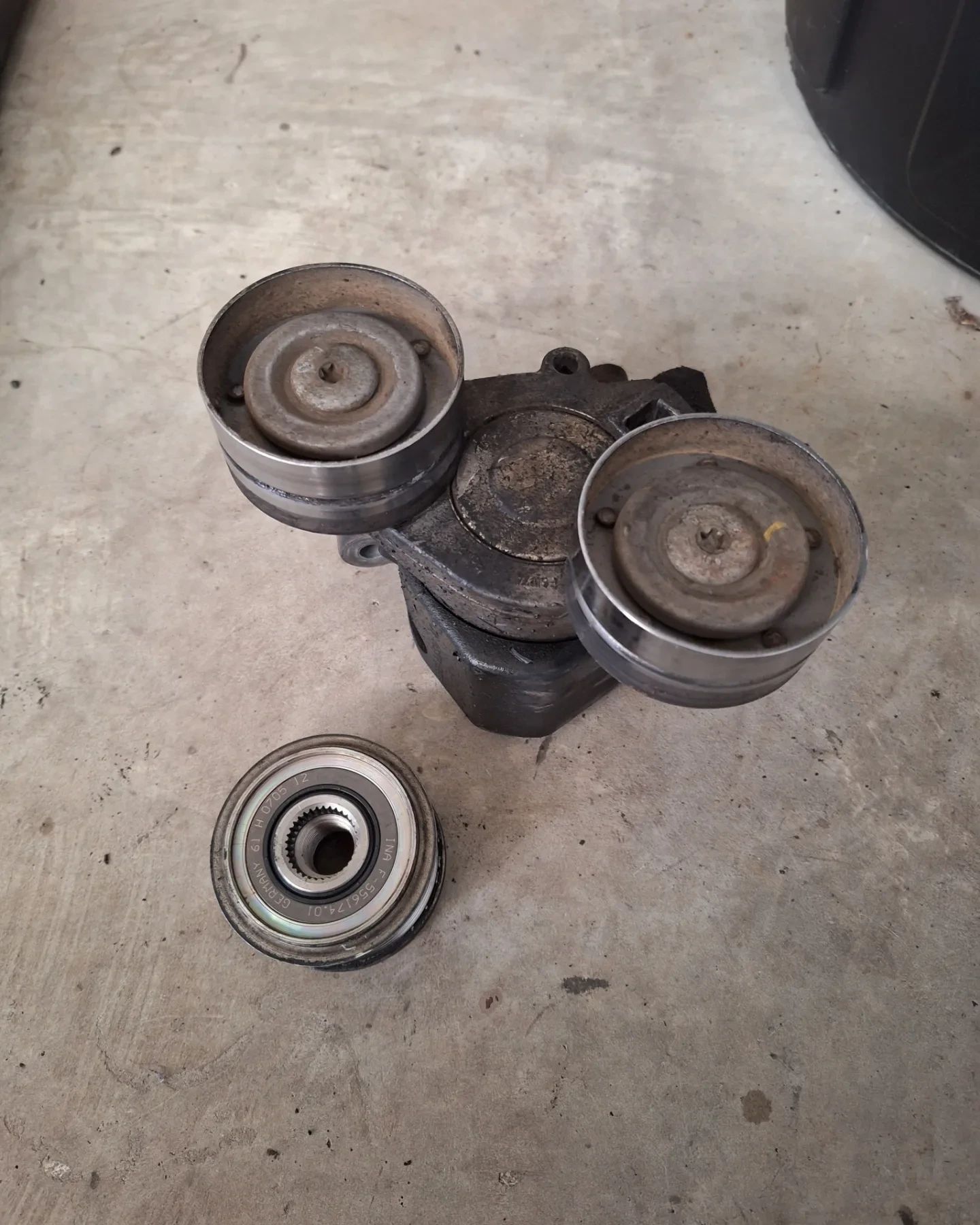 A belt tensioner is sitting on the ground next to a bearing.