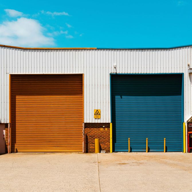 Two closed warehouse doors, one orange and one blue, on a white industrial building