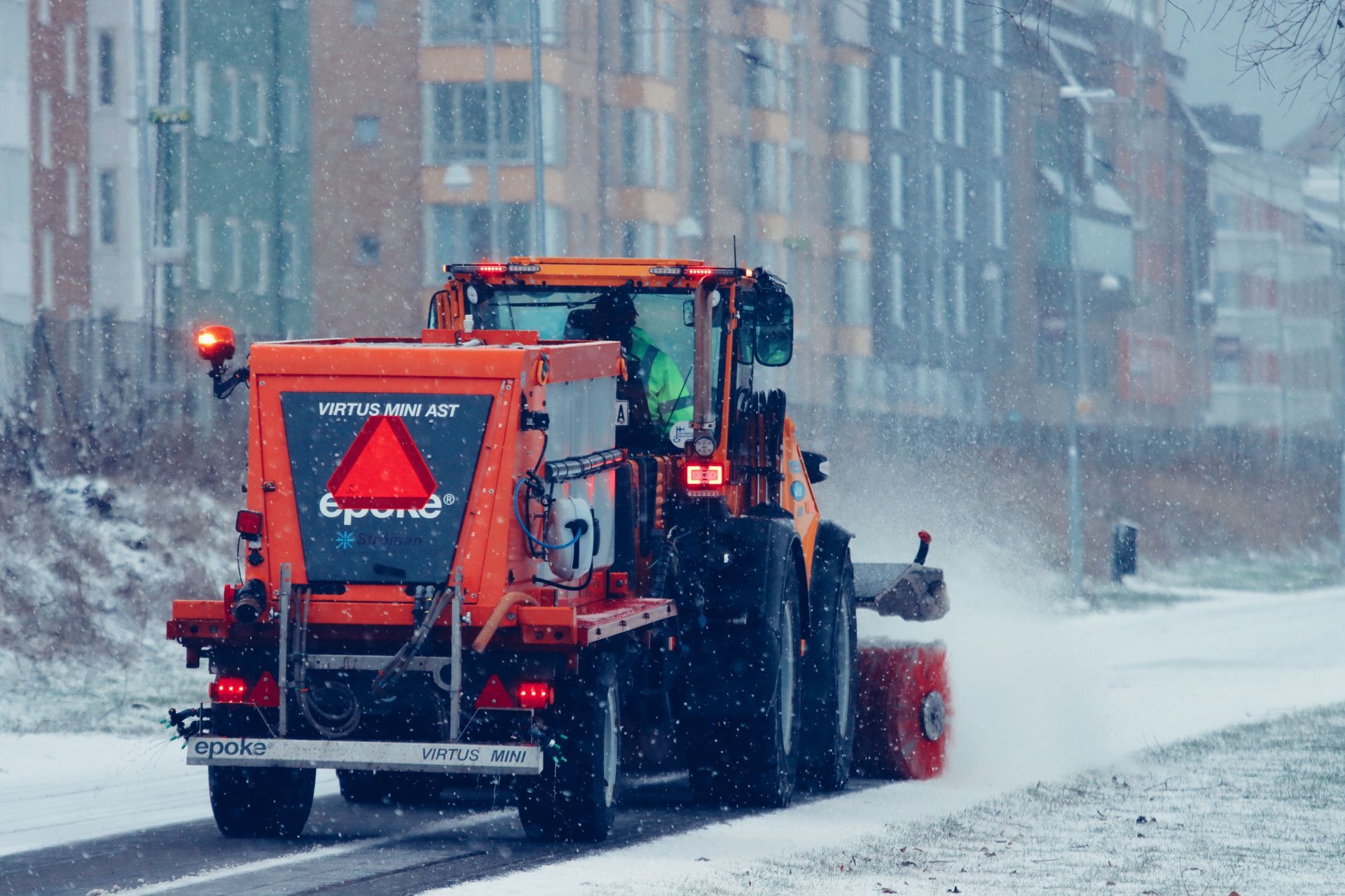 Orange snowplow clearing a snowy city street during a snowstorm