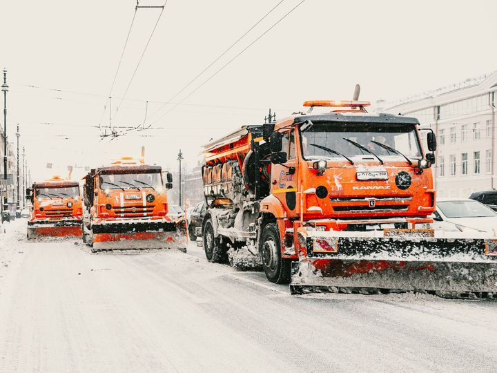 Orange snowplows clearing a snowy city street during a heavy snowfall