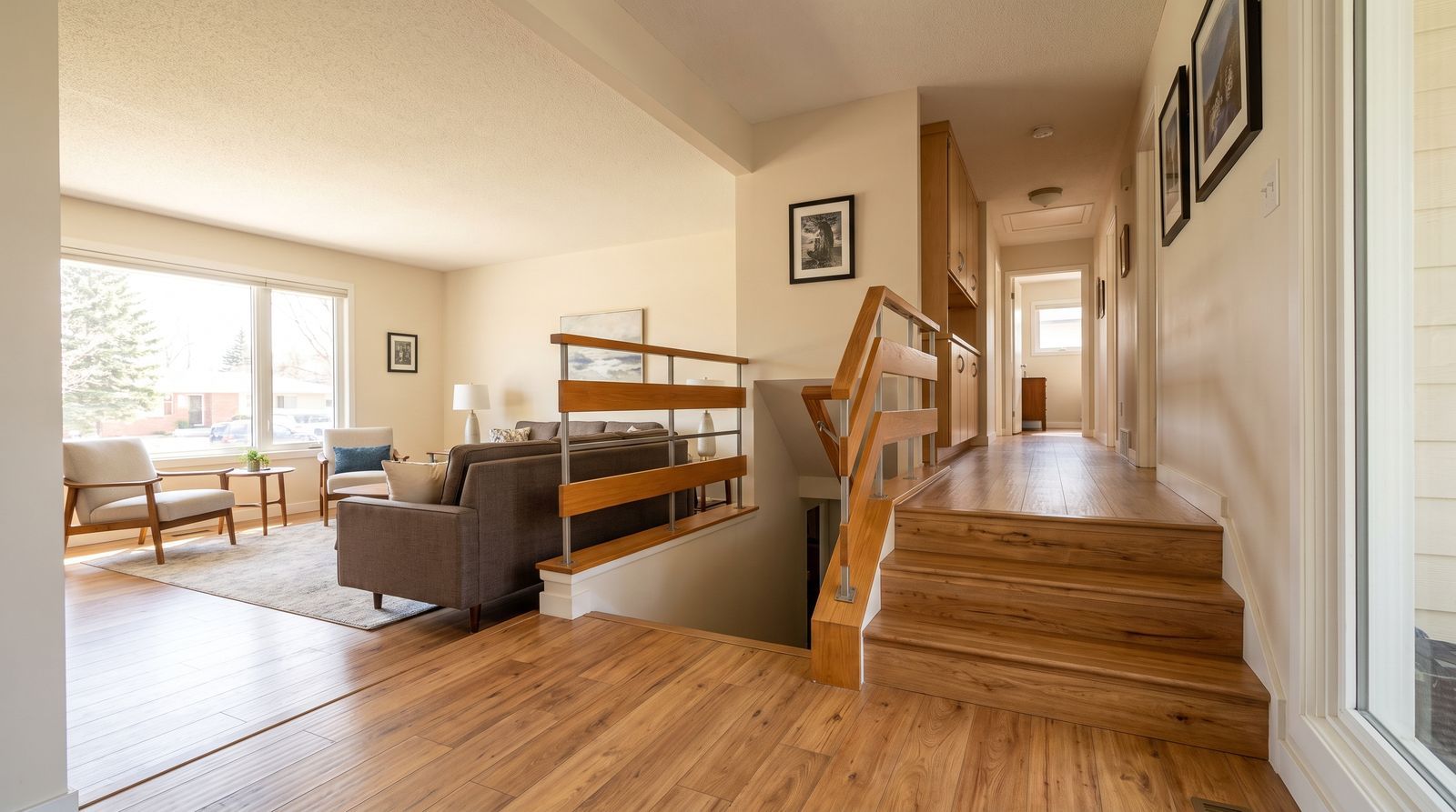 Bright living room with wood stairs, beige walls, hardwood floors, and a couch near a window.