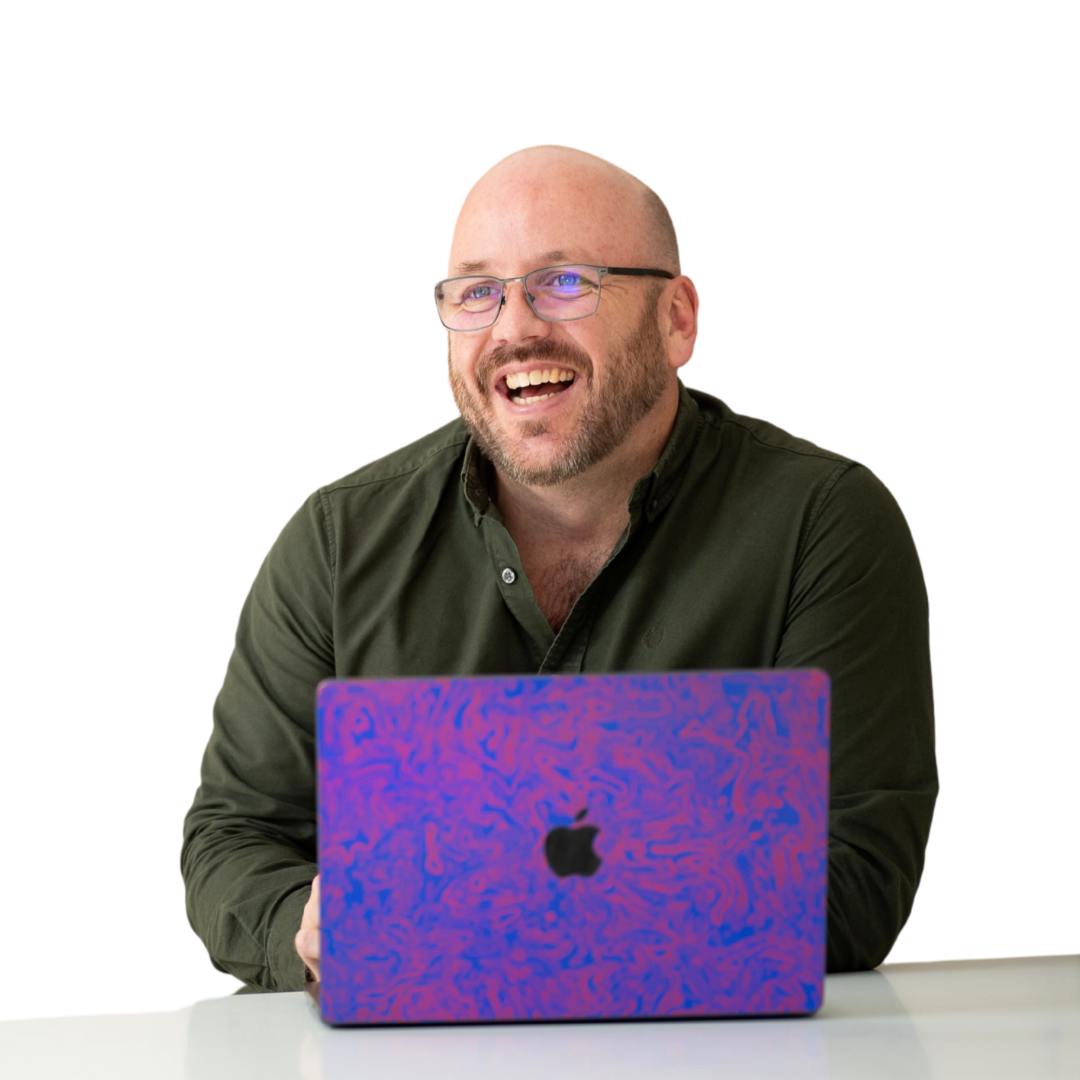 Smiling bald man in glasses behind a purple laptop at a white desk