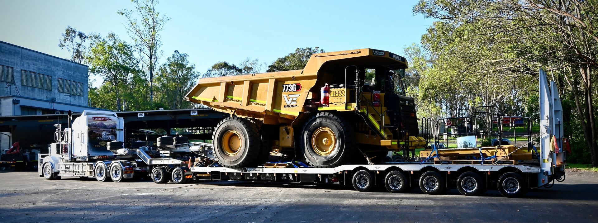 A large yellow Caterpillar dump truck being transported on a flatbed trailer, pulled by a semi truck.