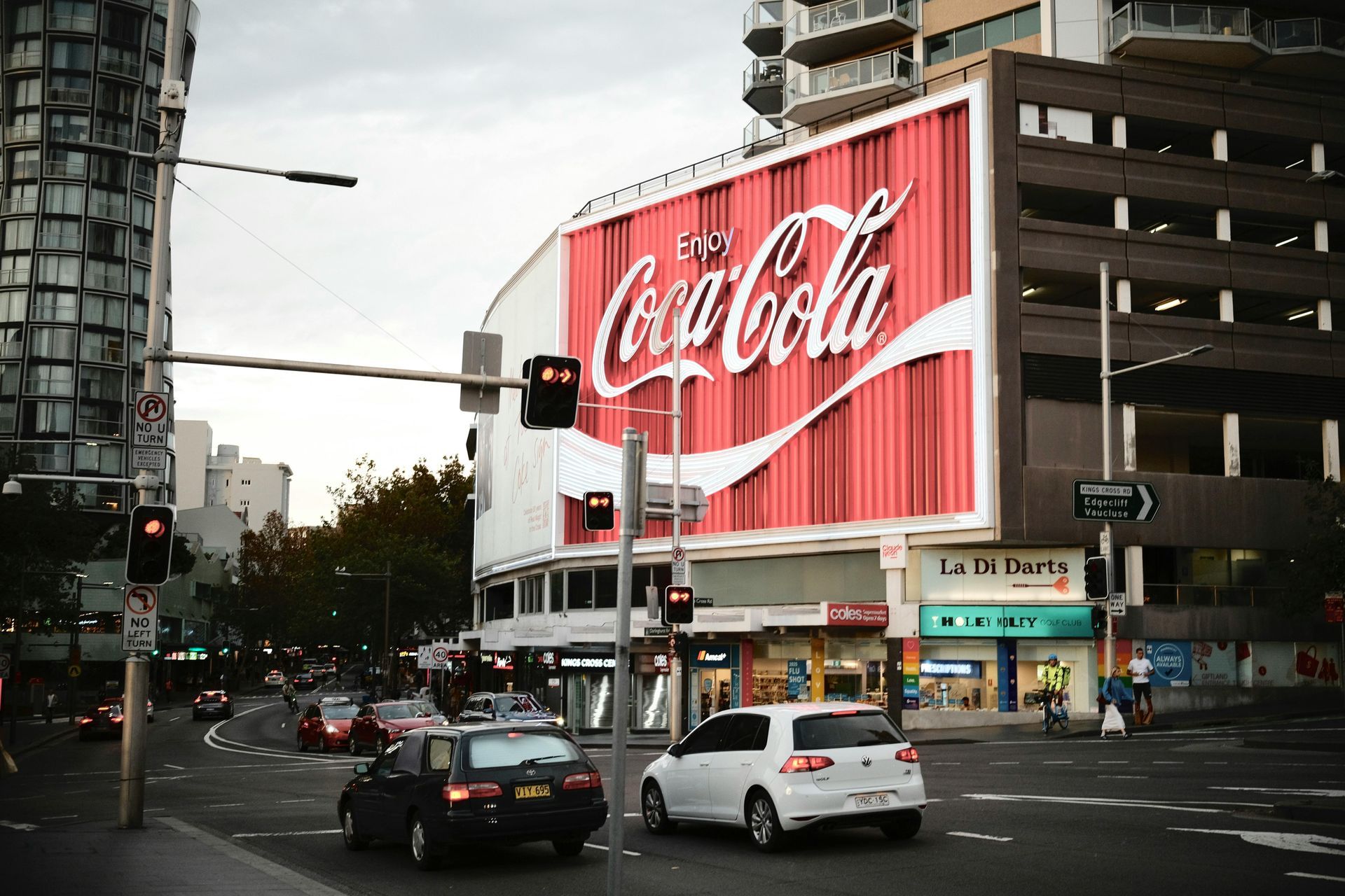 City street with a large red Coca-Cola billboard above traffic at dusk