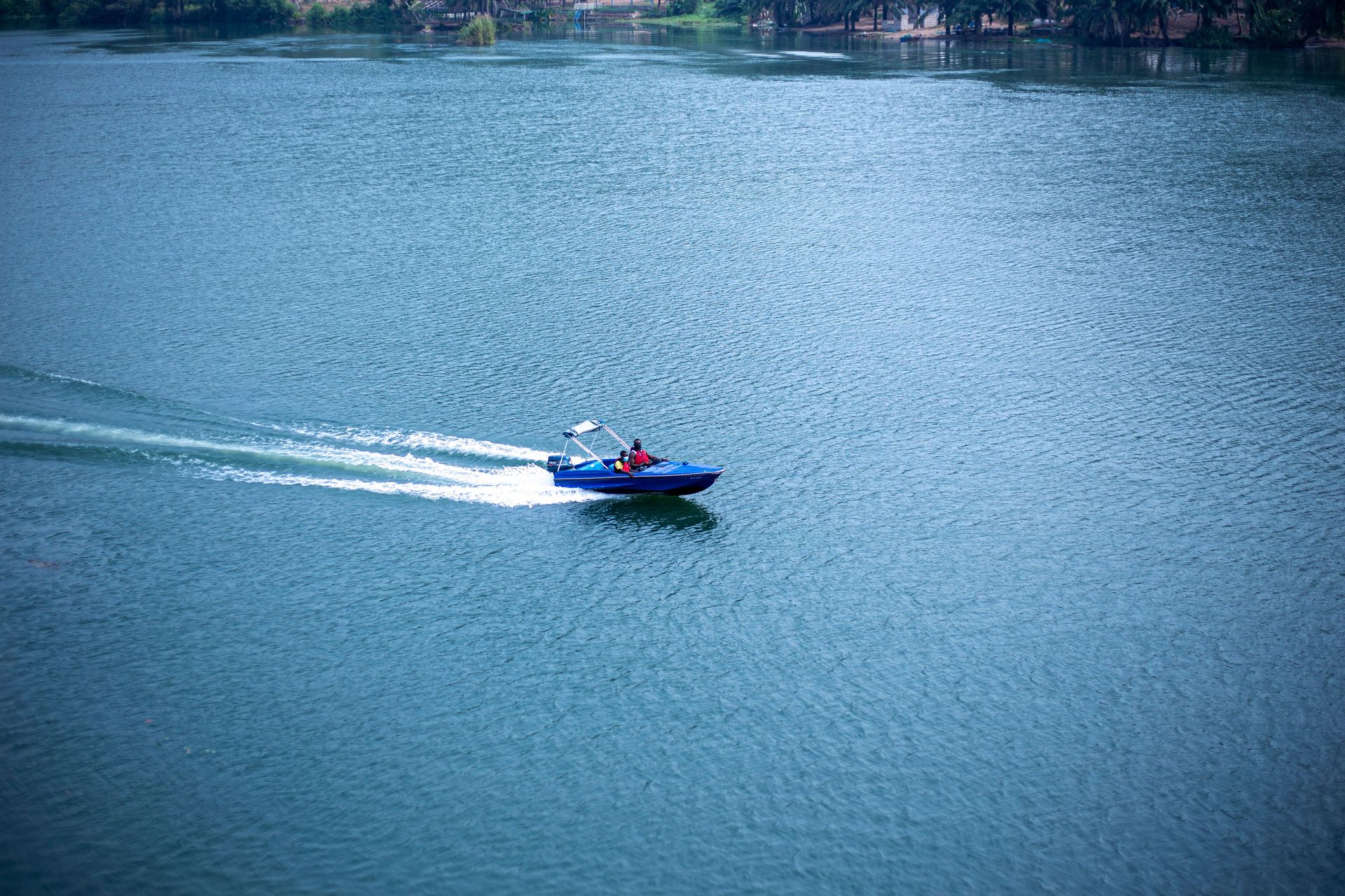 Small blue motorboat speeding across a lake, leaving a white wake behind.
