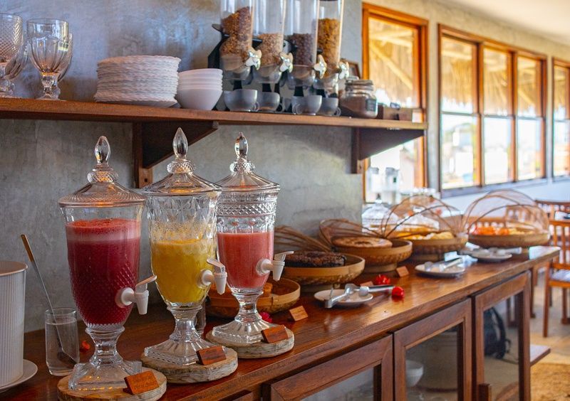 Um buffet de café da manhã com dispensadores de suco de vidro nas cores vermelha e amarela, dispensadores de cereais e pães em cestas.