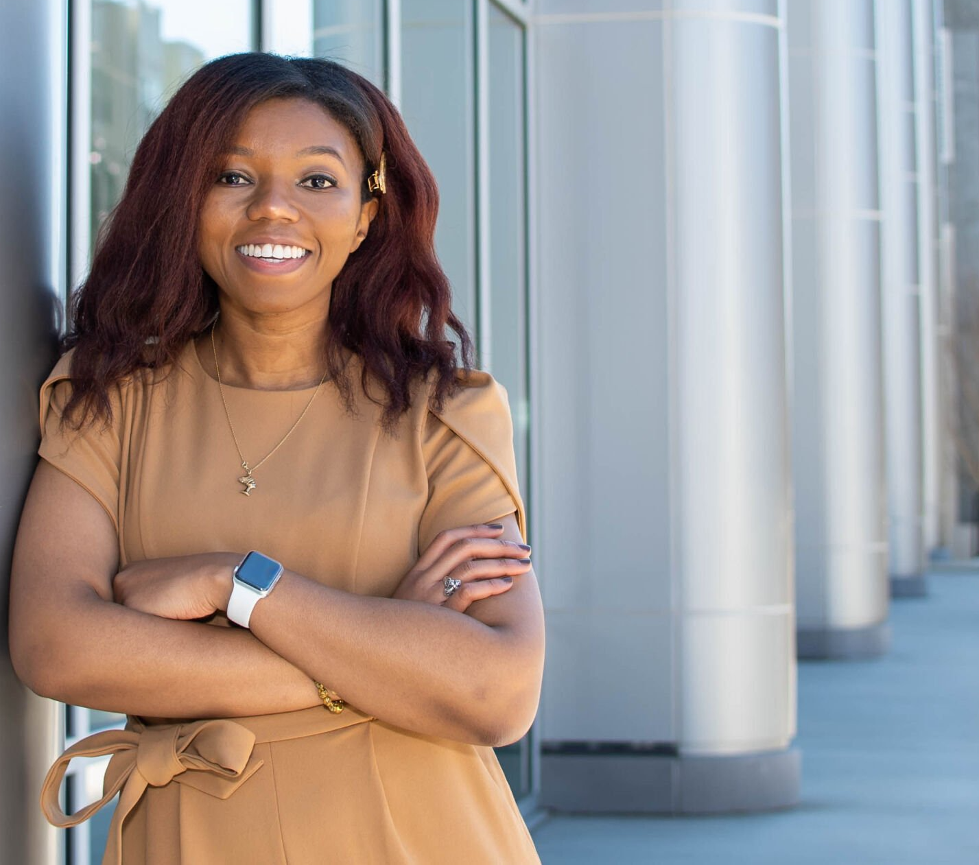 A woman is leaning against a wall with her arms crossed and smiling.