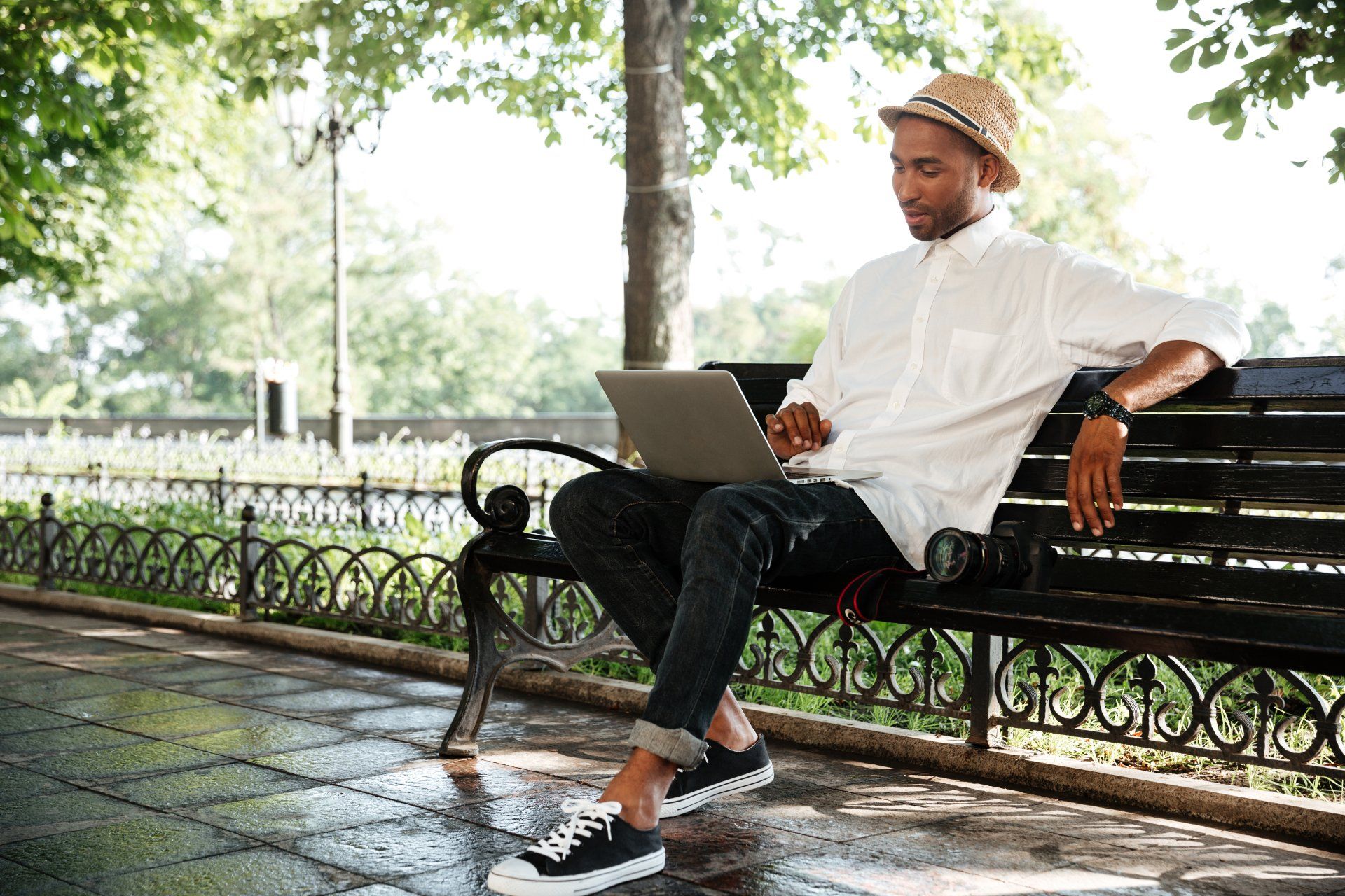 A man is sitting on a park bench using a laptop computer.