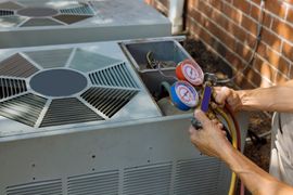 A technician uses a gauge manifold set to check the pressure of an outdoor air conditioning unit.