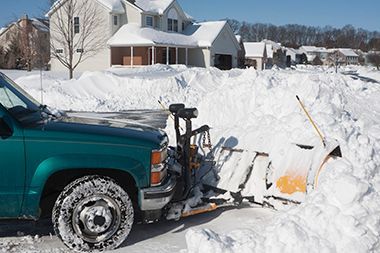 A snow plow is clearing snow from a driveway in front of a house.