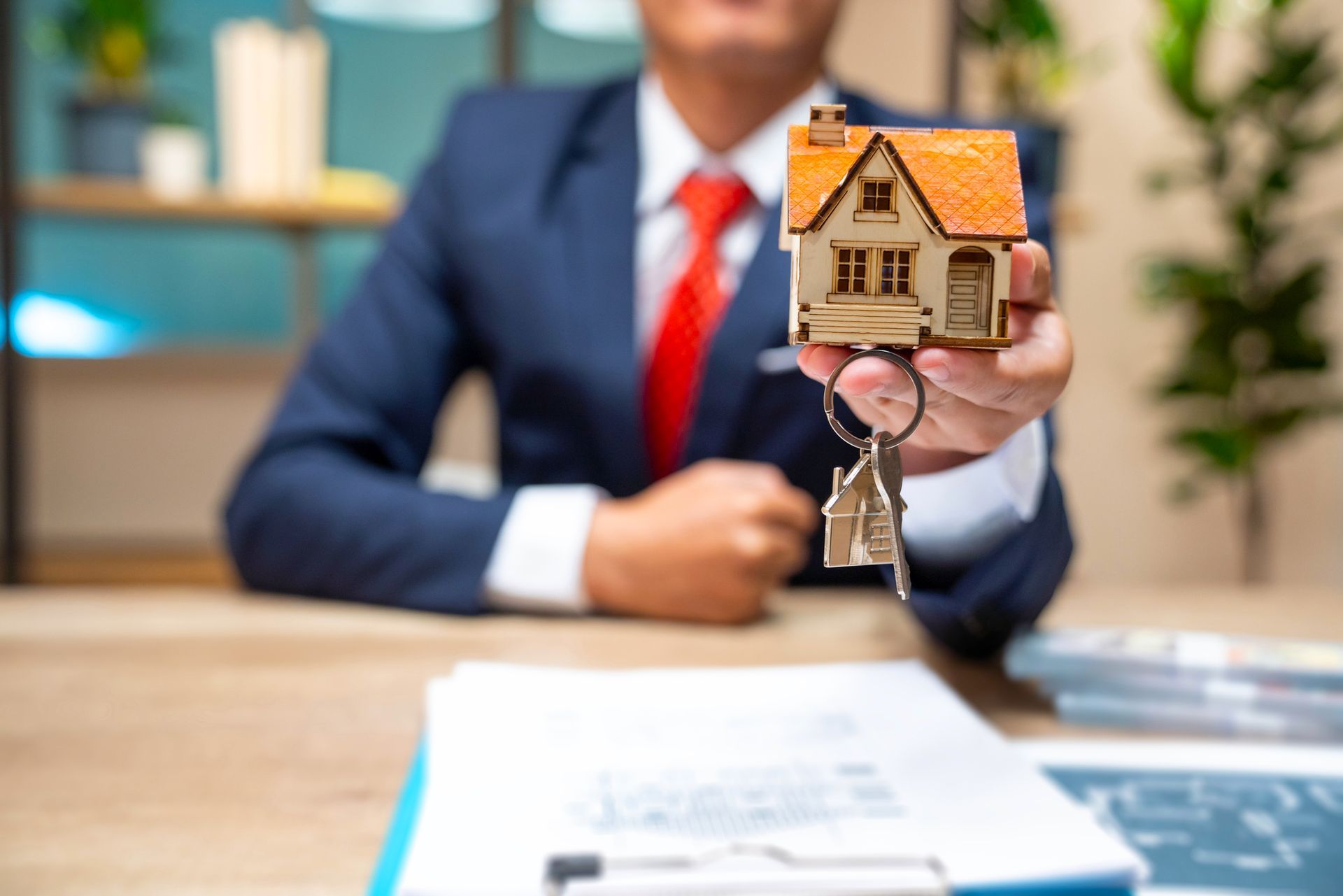 A man in a suit and tie is holding a model house and keys.