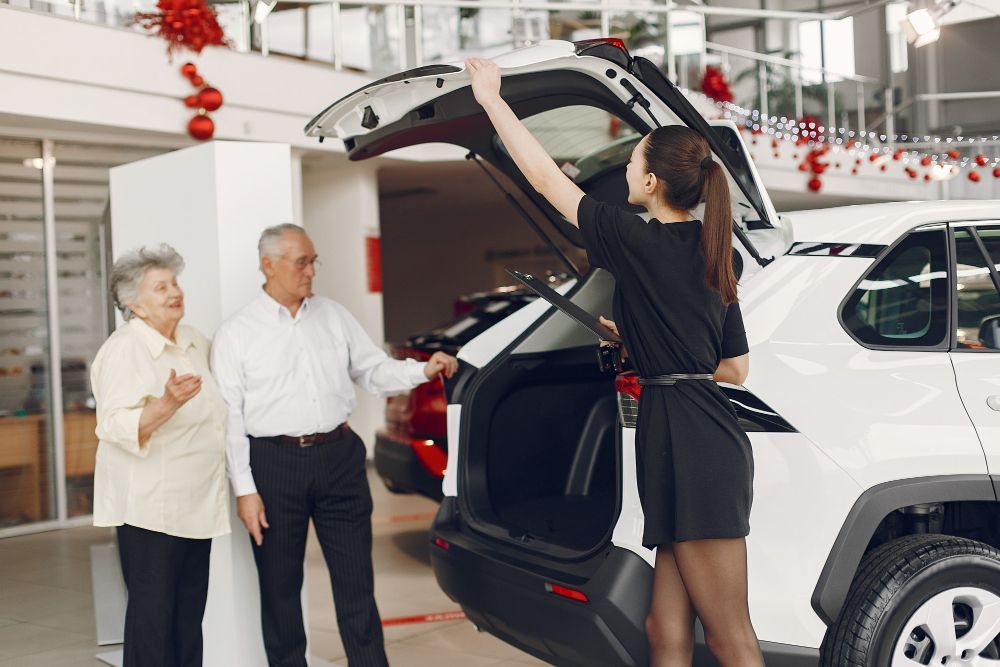 Un vendedor carga equipaje en un SUV blanco mientras dos clientes observan en una sala de exposición.