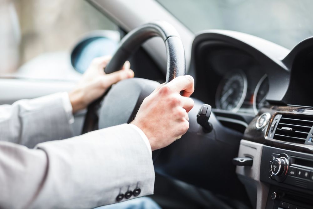 Manos del conductor en el volante dentro de un automóvil, con el tablero y la consola central visibles.