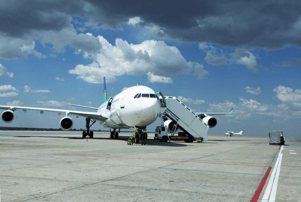 Gran avión de pasajeros blanco en la pista con escaleras de embarque bajo un cielo azul nublado.