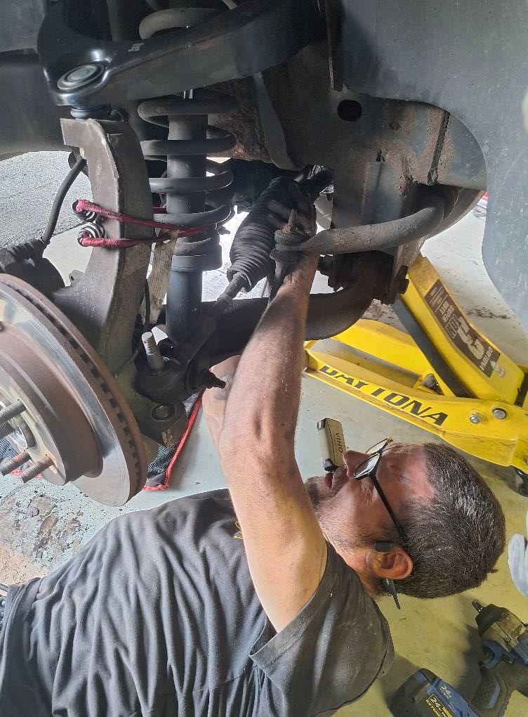 Mechanic works on a car's suspension system. He lies on the ground, tools nearby, near a yellow jack.