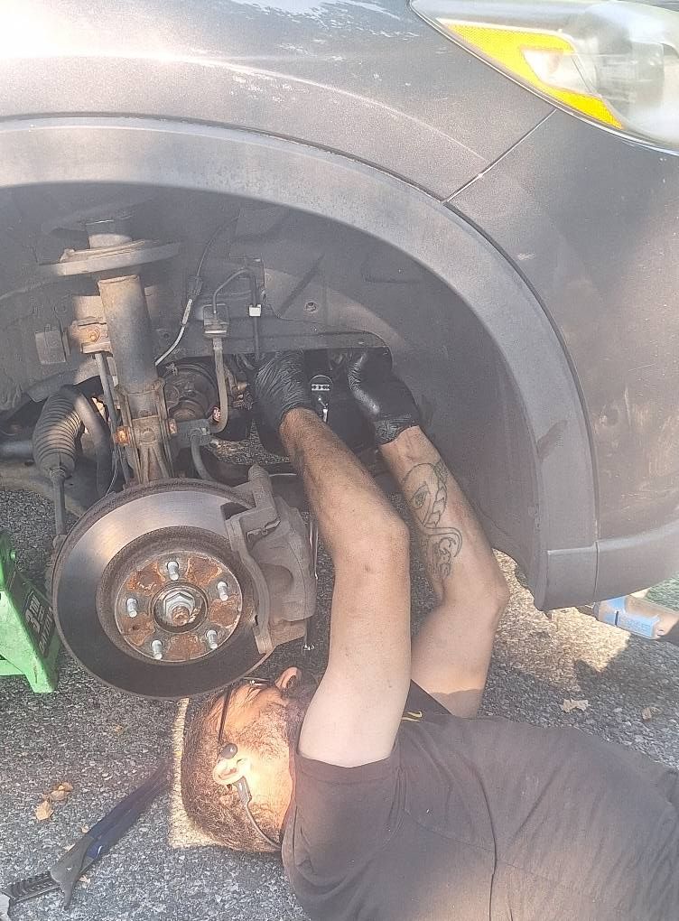 Person working on a car. The person is lying on the ground under the front wheel.