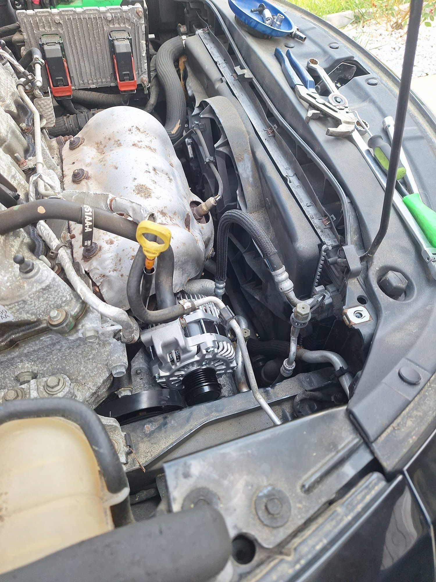 Car engine bay with parts visible: radiator, fan, alternator, belts, and various tools.