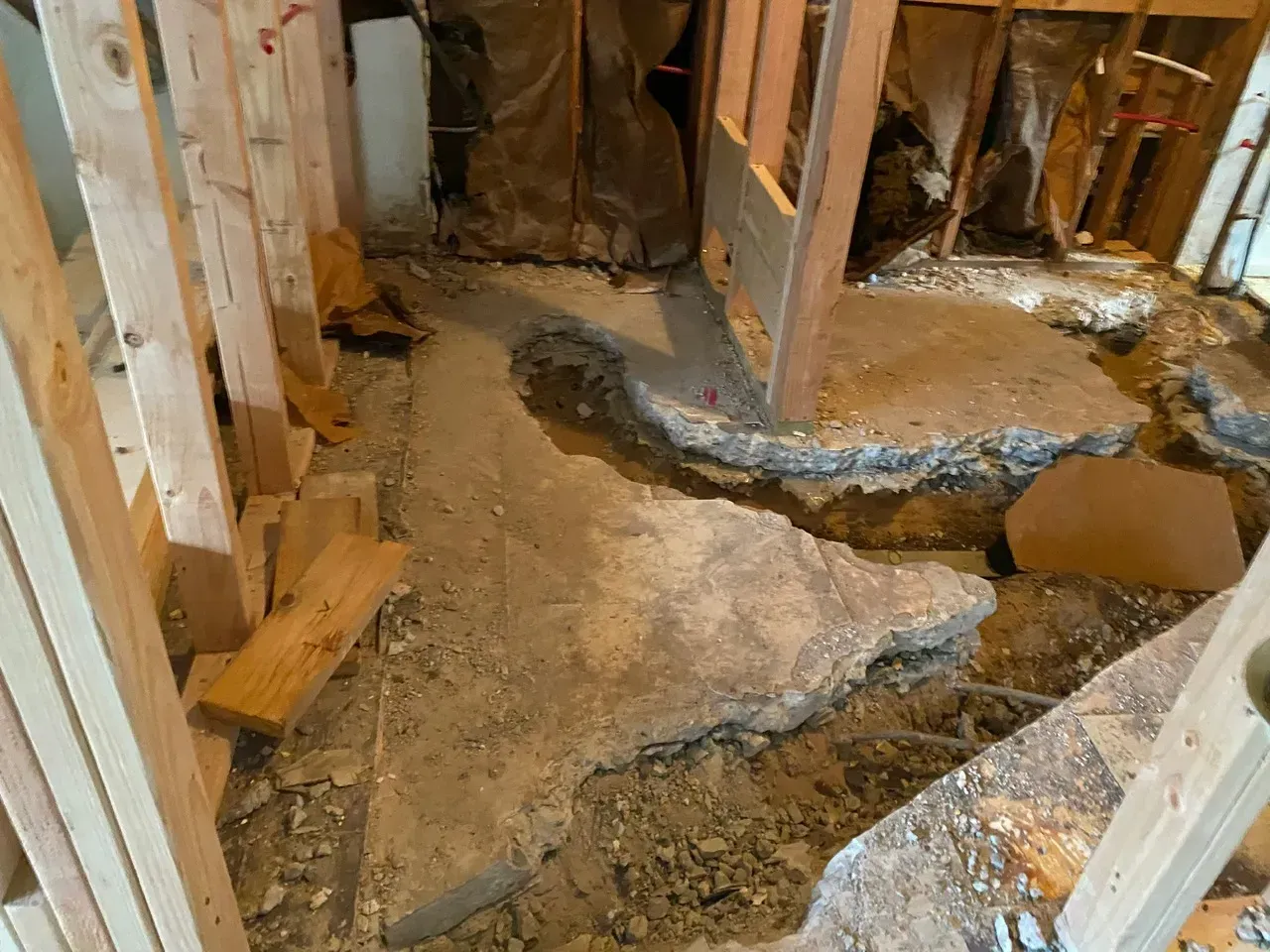 Damaged concrete floor in a room under construction, surrounded by exposed wooden framing and debris.