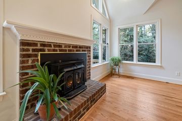 Bright living room with brick fireplace, hardwood floors, and large windows overlooking trees