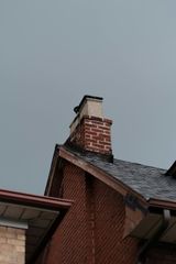 Red brick house roof with chimney against a gray sky