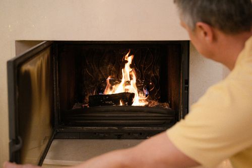Man in yellow shirt tending a lit fireplace with open glass doors
