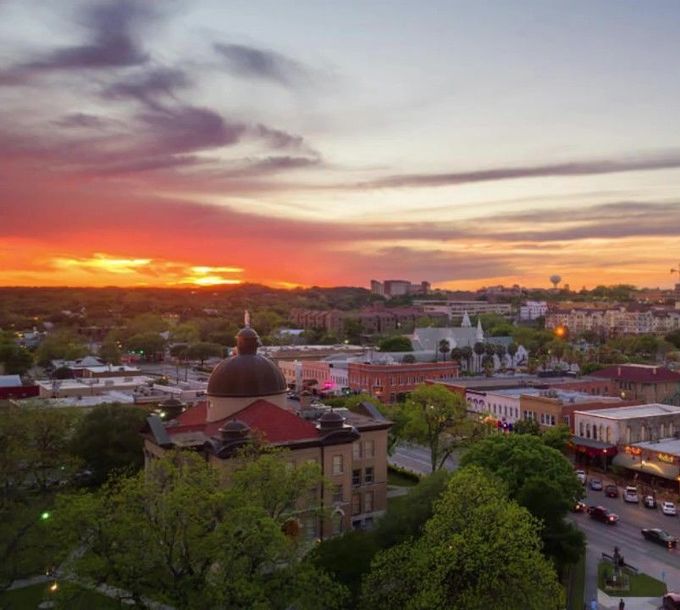 Sunset over a city skyline with a domed building in the foreground and colorful sky.