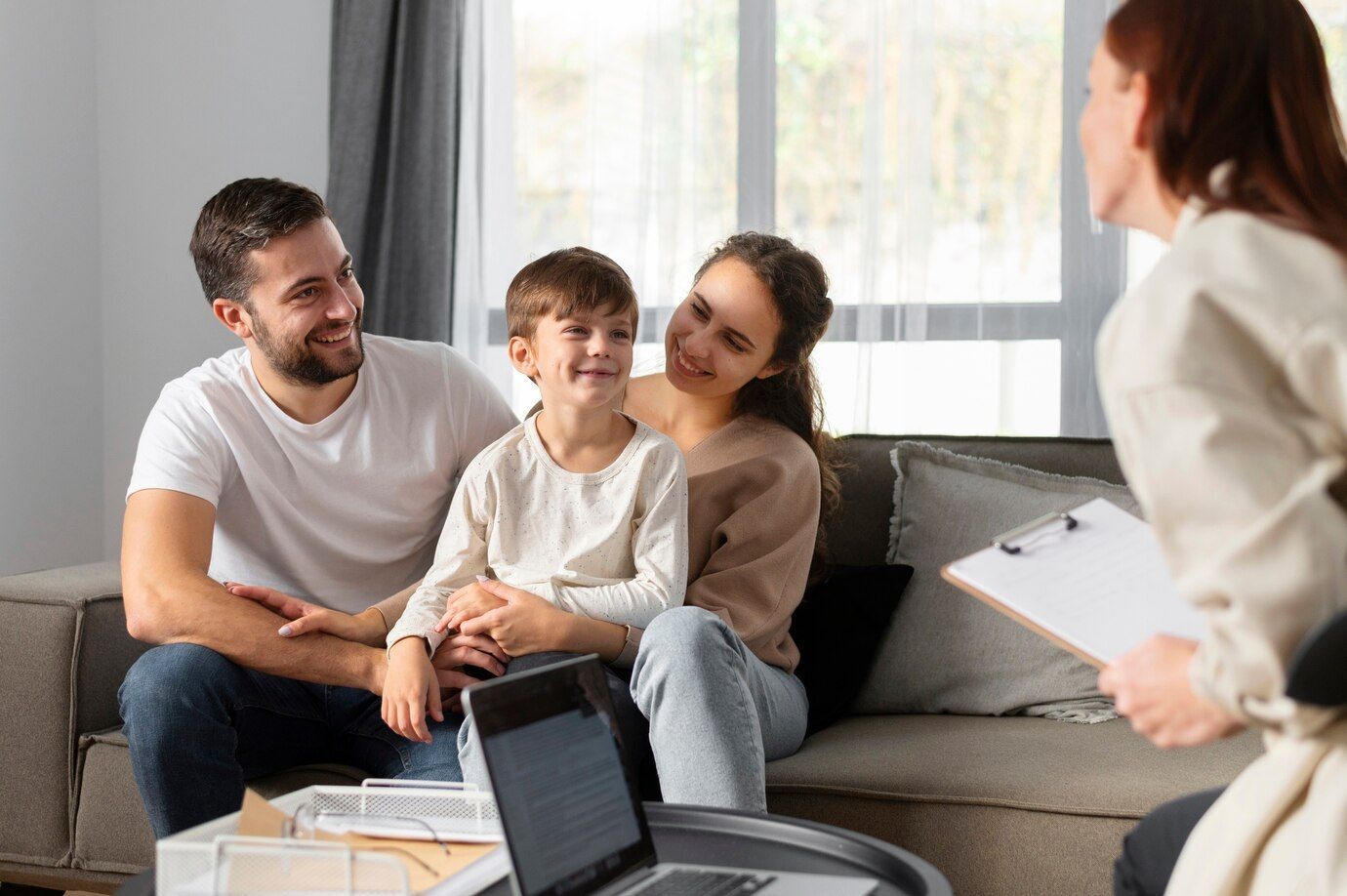 Family smiles while sitting on a couch, talking to a person with a clipboard.
