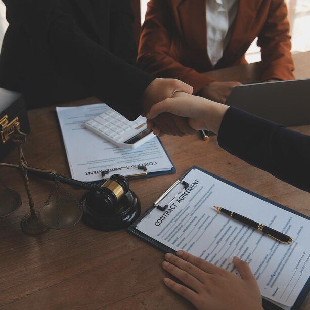 People shaking hands over contract documents at a law office table.