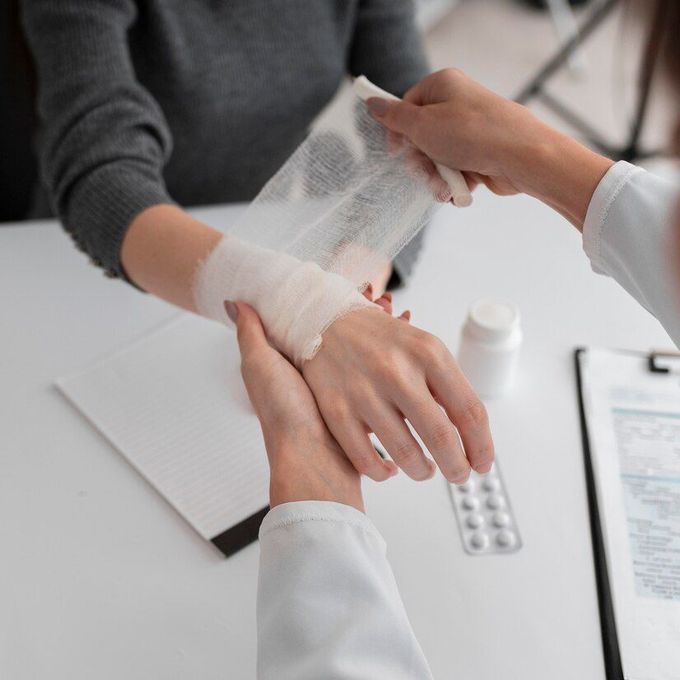 Person receiving a bandage on their wrist from another person in a white coat.
