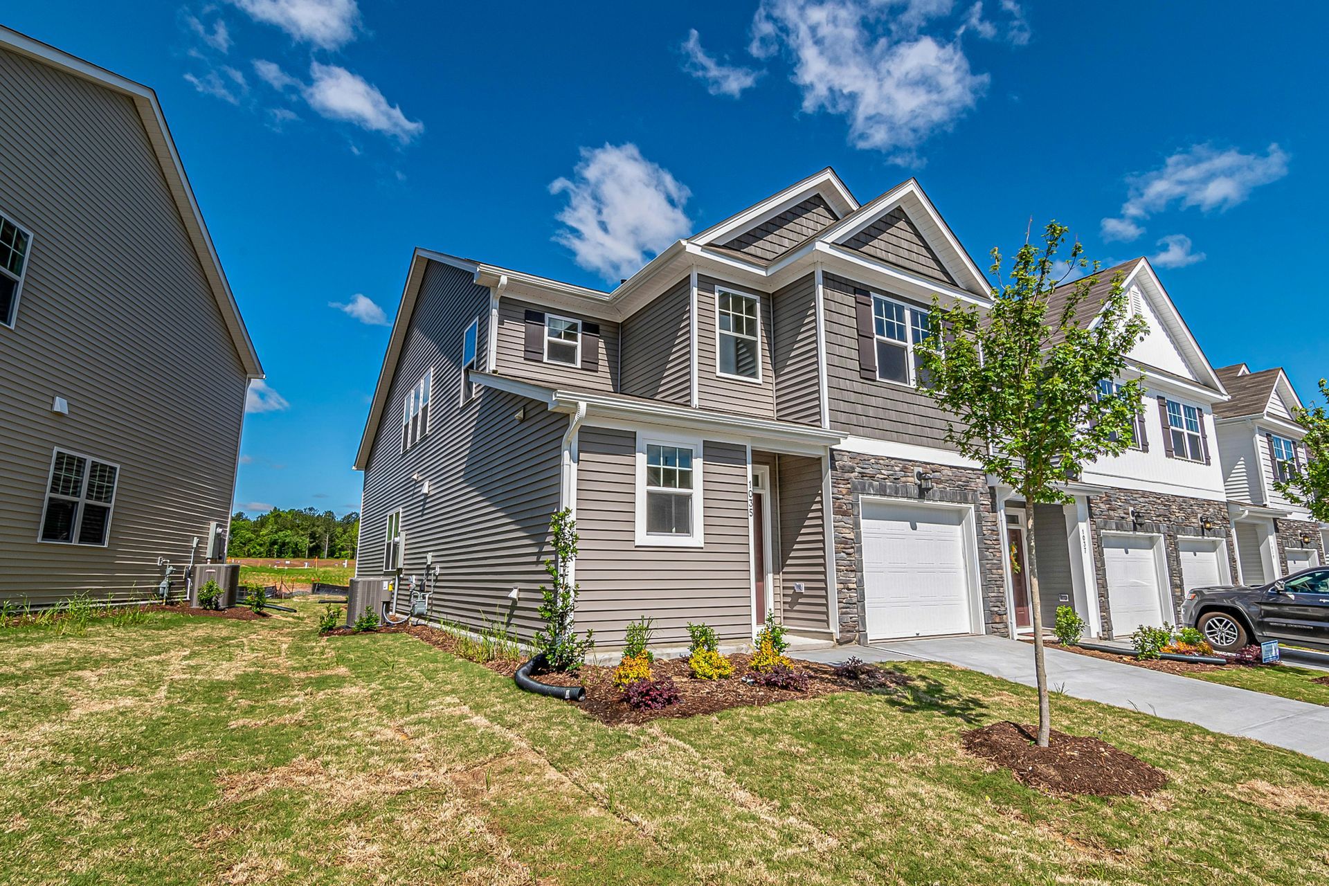 Gray and white multi-story houses with blue sky and green grass.
