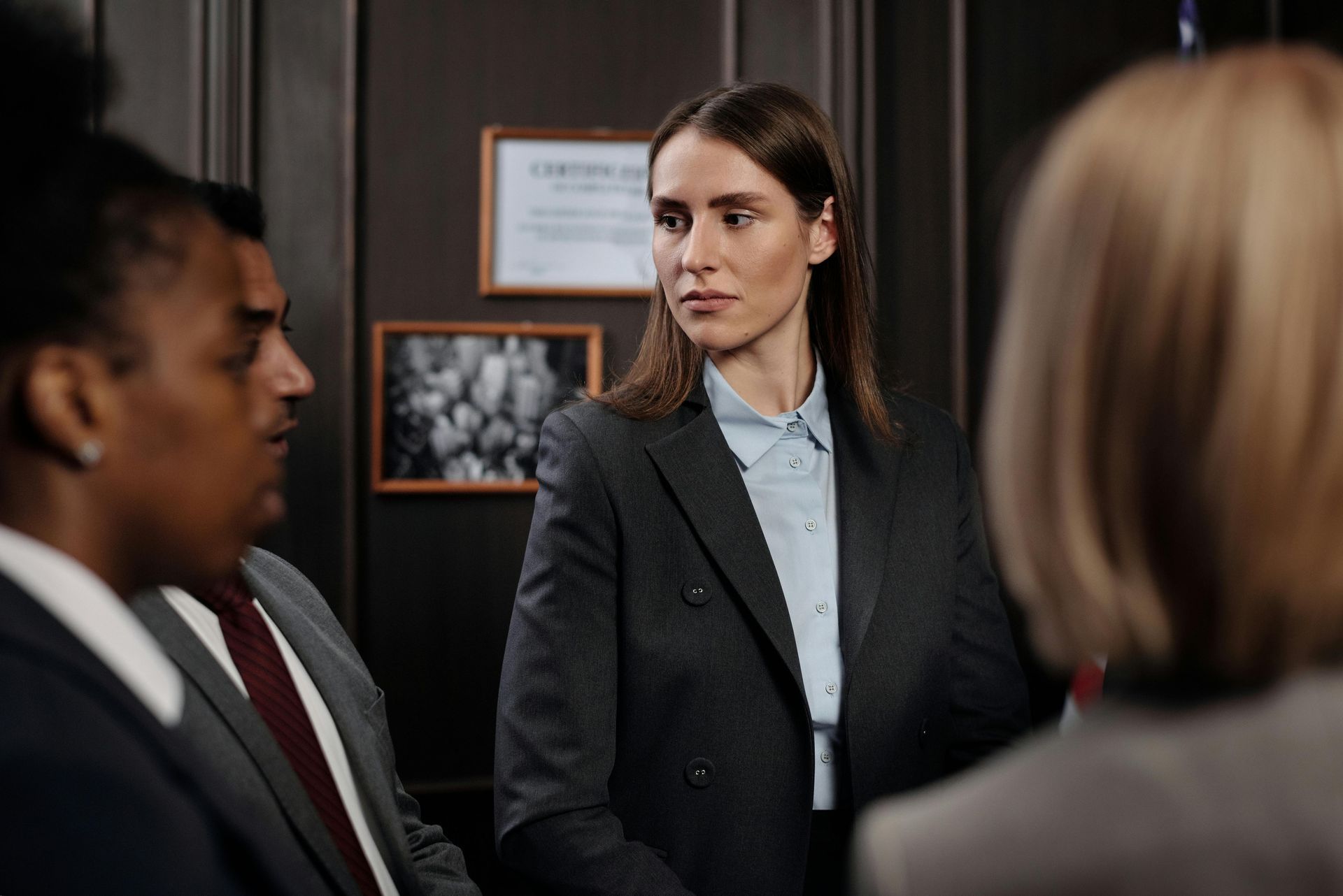A woman in a suit looks at a group of people. Other people in suits are in the foreground.