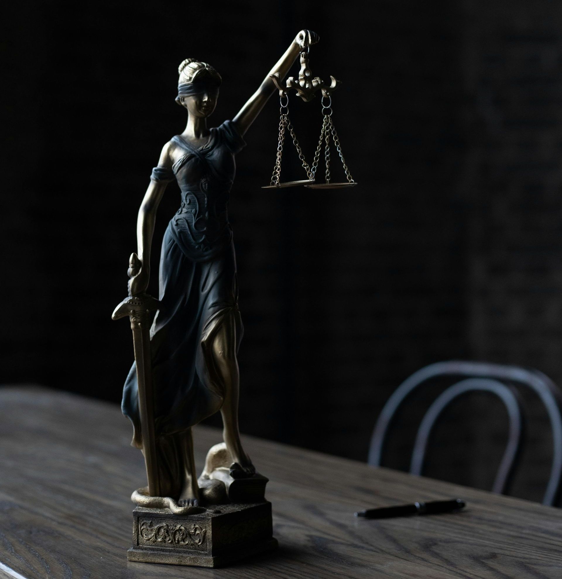 Statue of Lady Justice holding scales and sword on a wooden table. Dark setting.