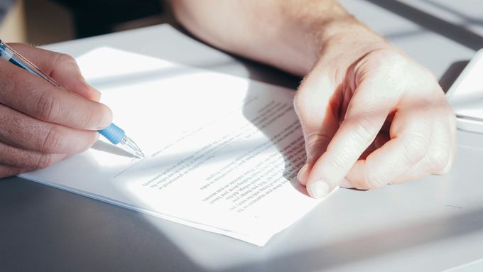 Hands holding a pen, signing a document on a desk, close-up shot.