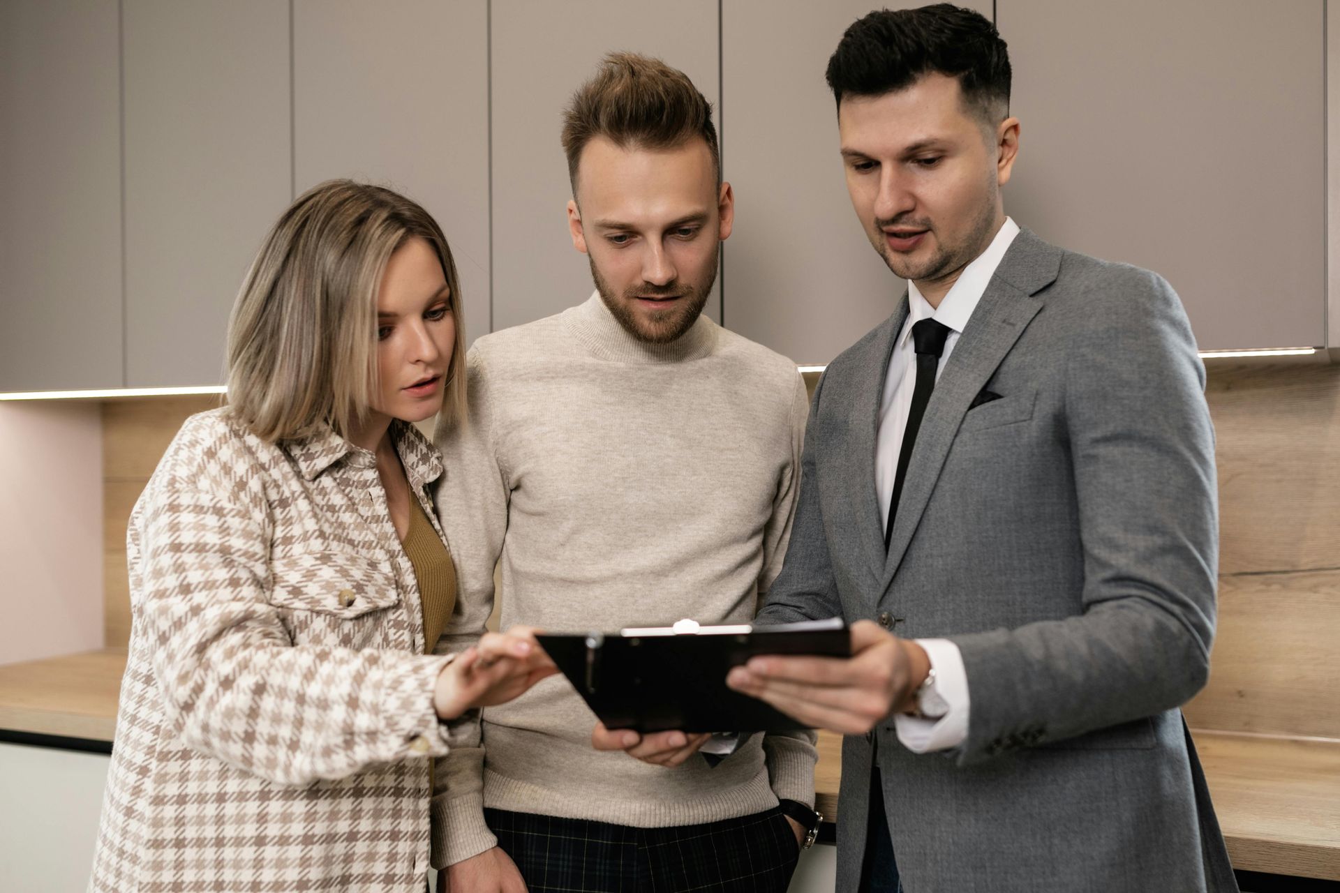 Real estate agent showing paperwork to a couple in a modern kitchen.