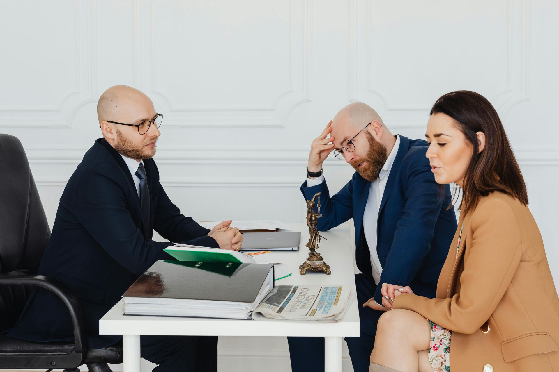 Lawyer advising a couple at a table. The man leans on his head, and the woman looks concerned.