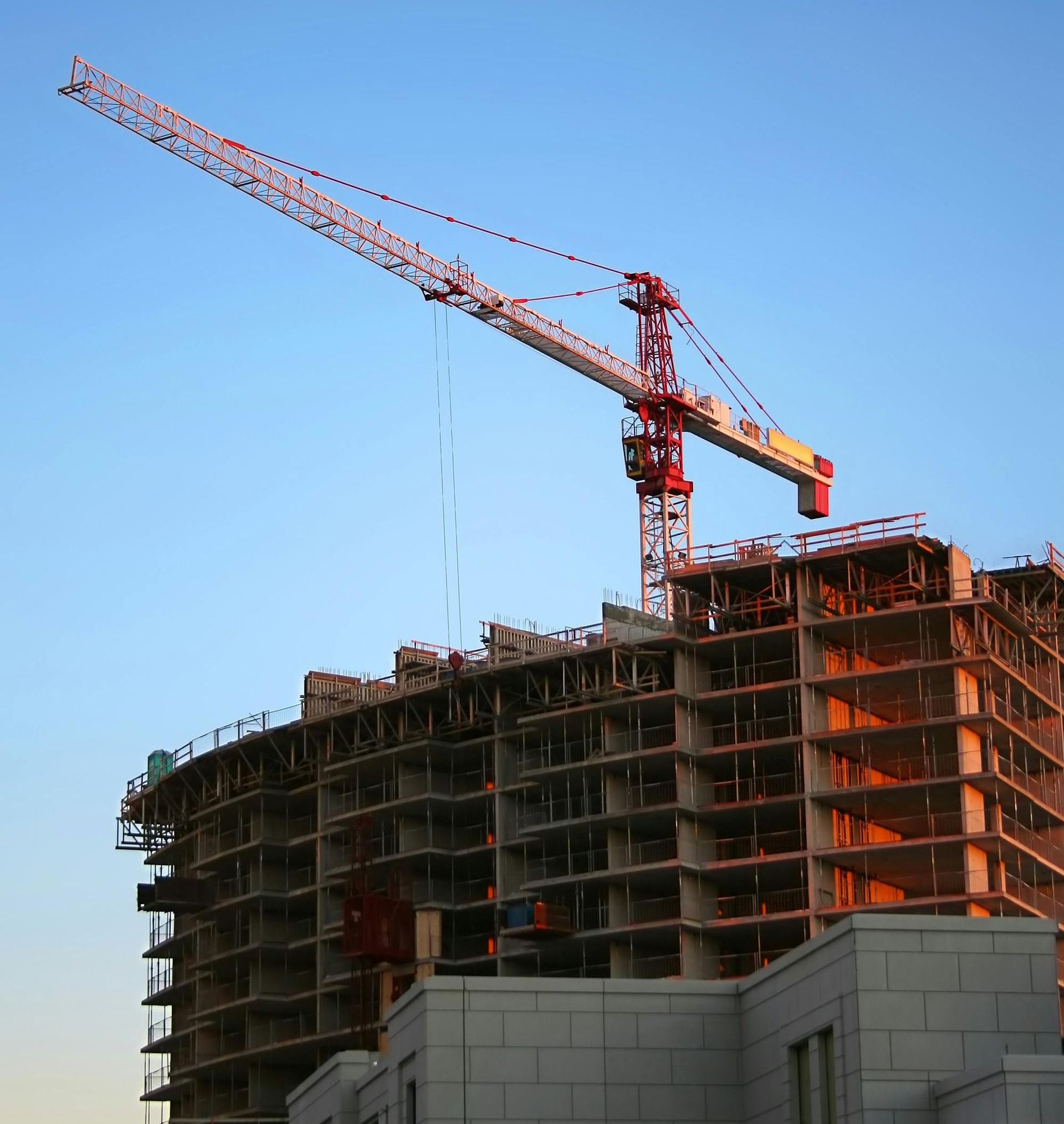 Construction crane atop a building under construction against a clear blue sky.