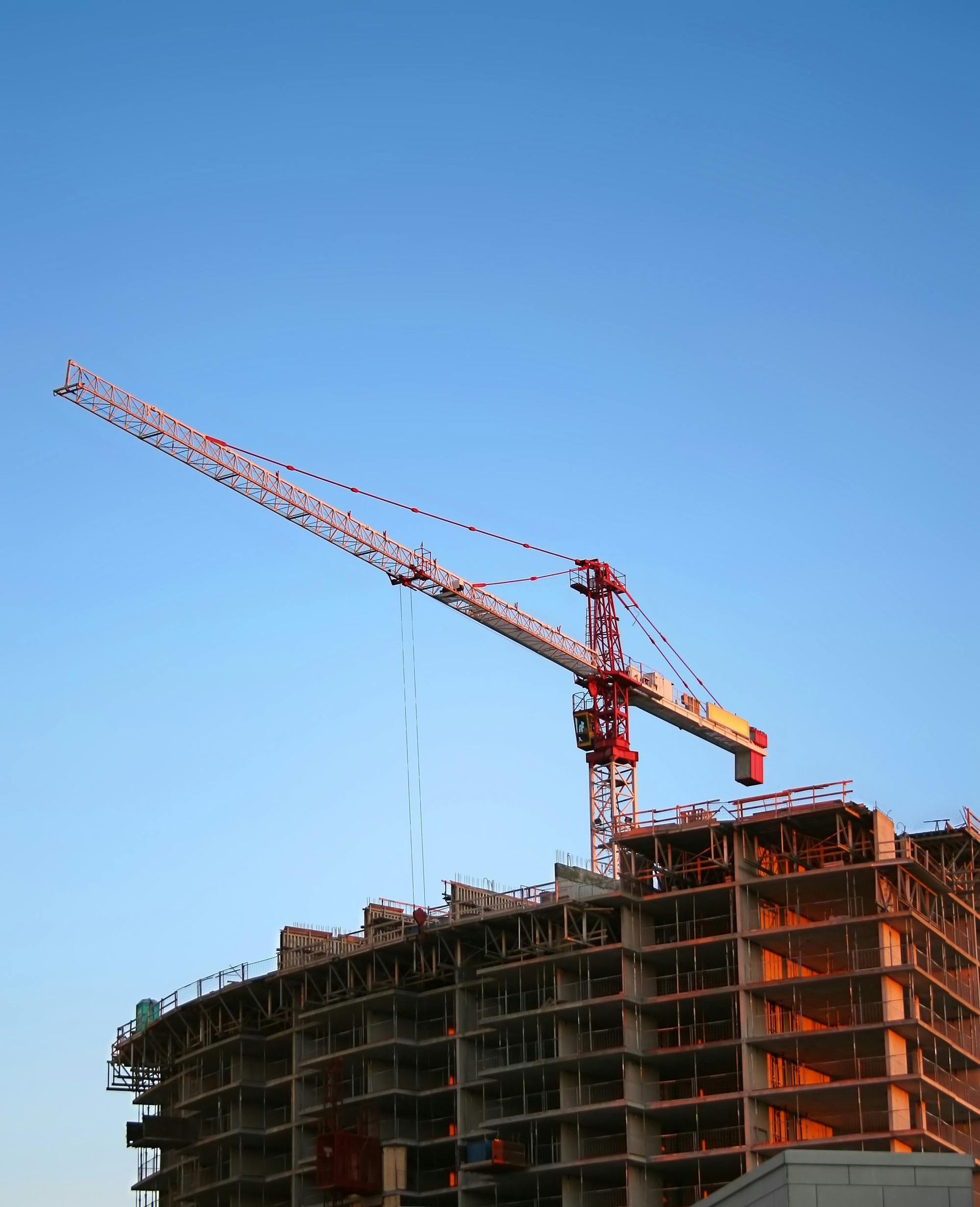 Construction crane over a multi-story building under construction against a clear blue sky.