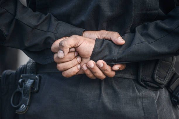 A man in a black jacket is standing with his hands behind his back.
