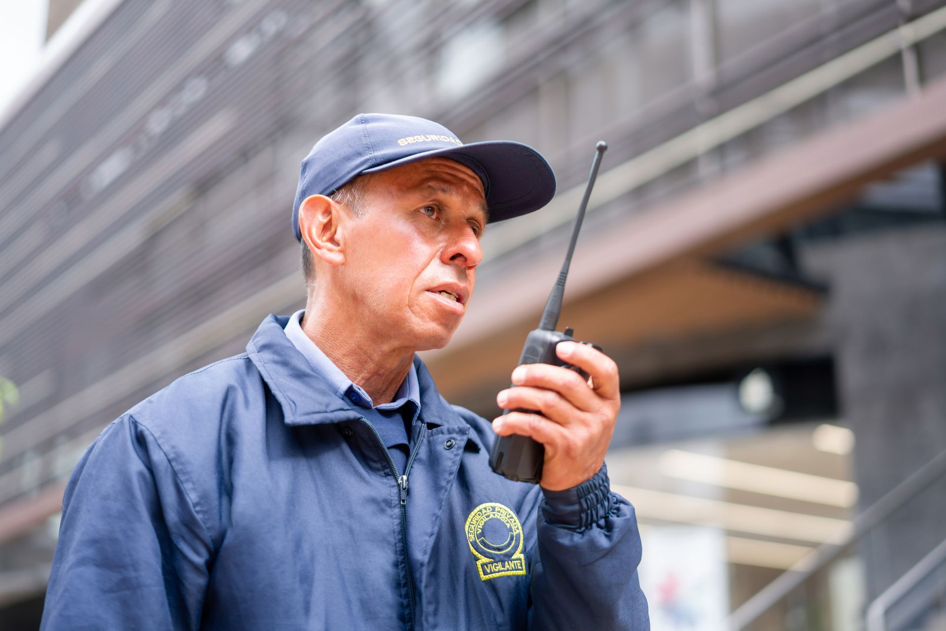 A man in a blue jacket and hat is talking on a walkie talkie.