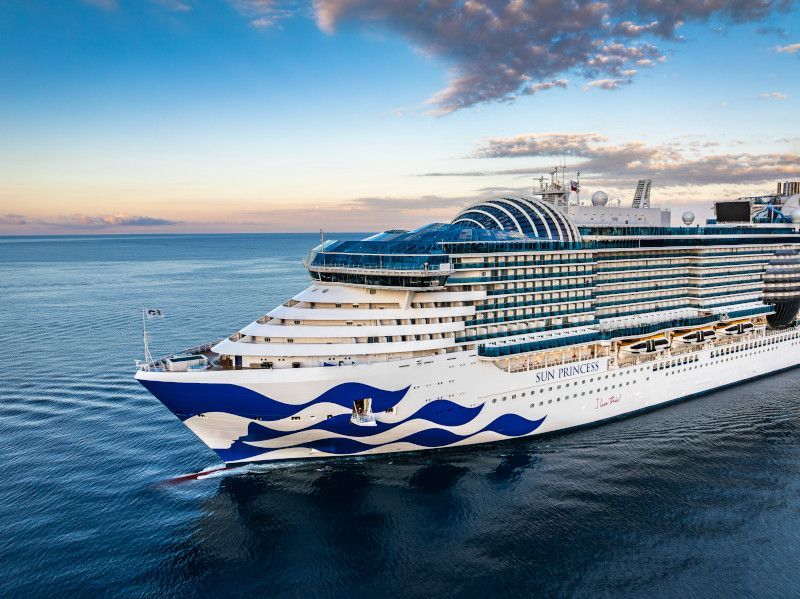 Large white-and-blue cruise ship sailing on calm ocean at sunset