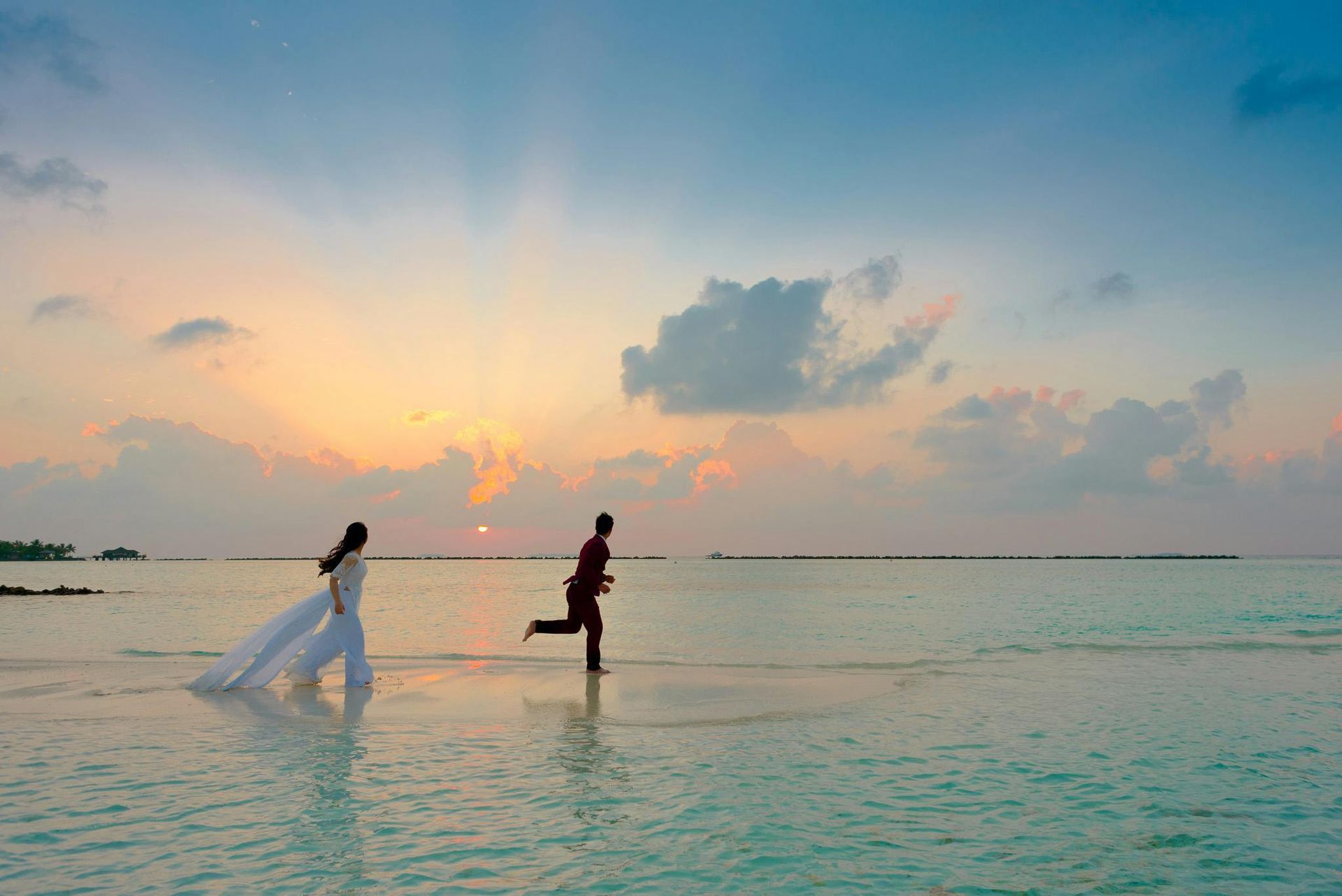 Two people running through shallow water at sunset under a pastel sky