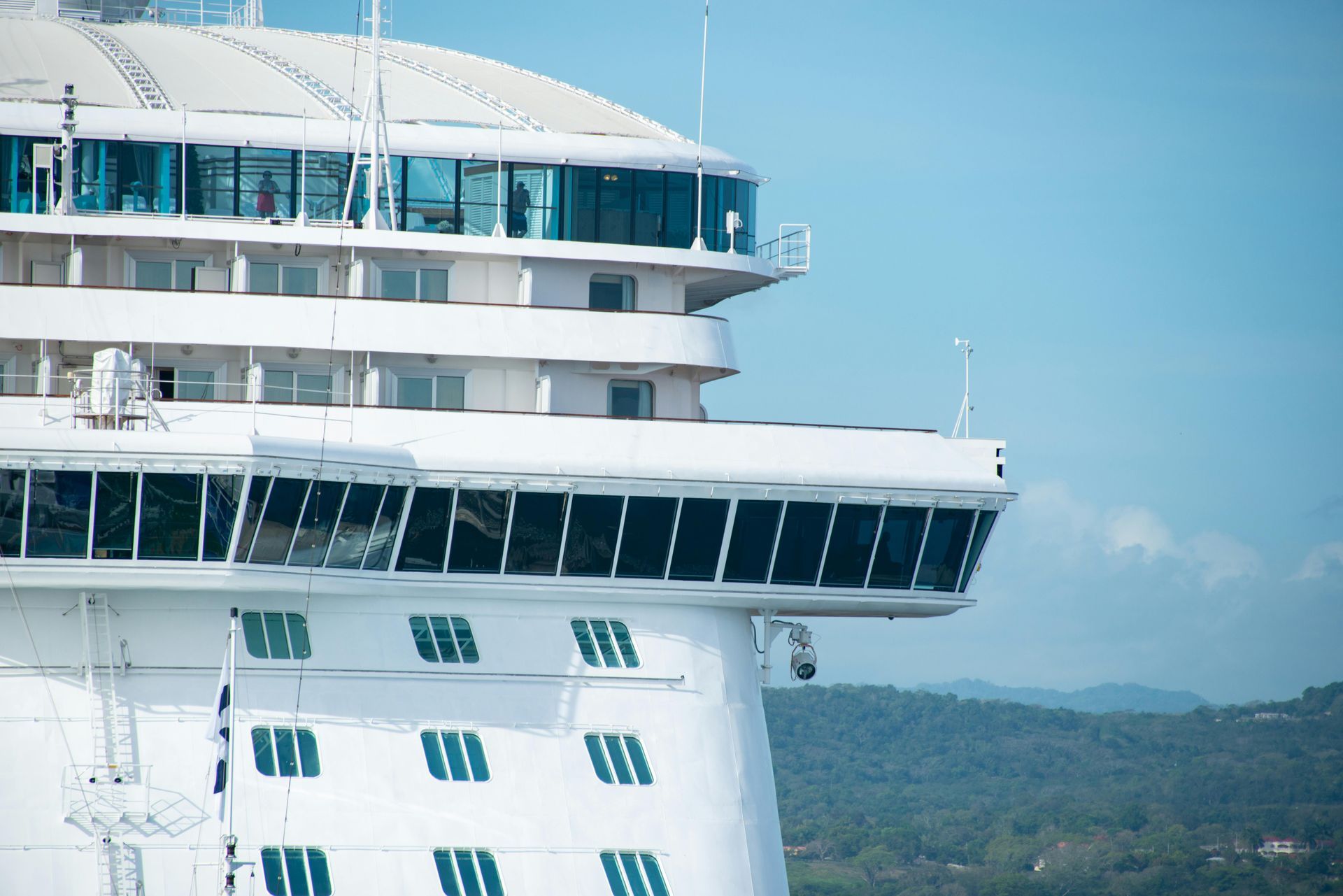 Close-up of a white cruise ship bridge overlooking the sea and distant green hills