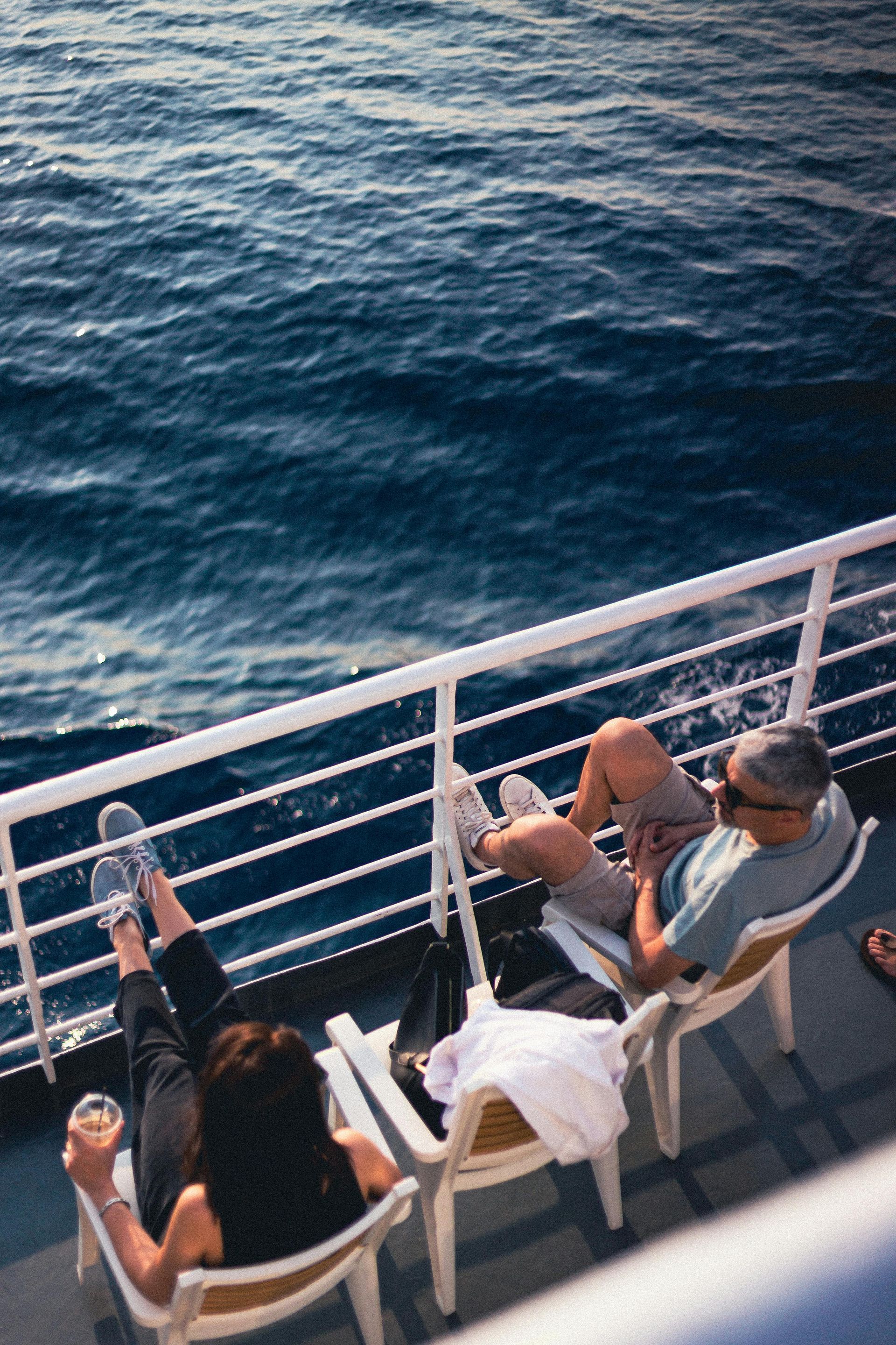 Two people relaxing on a boat deck, one holding a drink, with the ocean beside them.