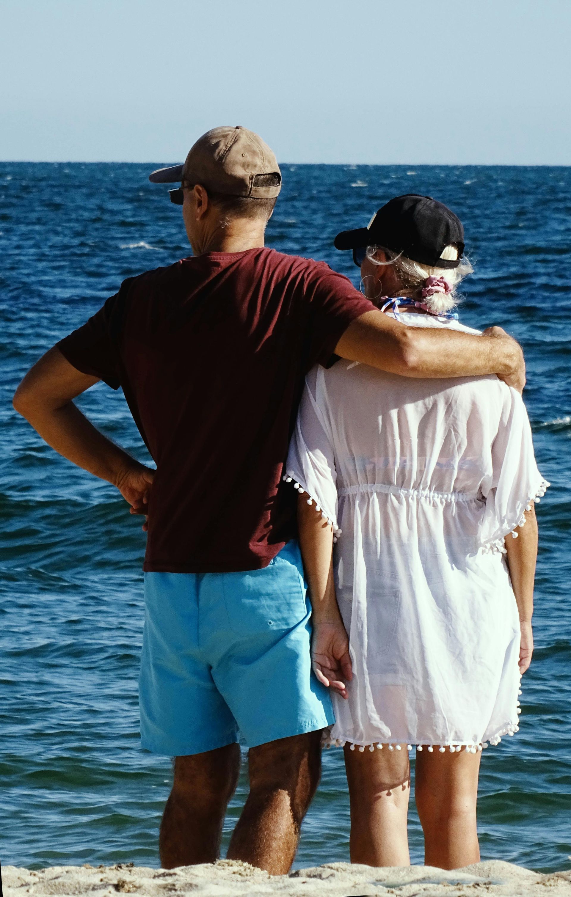 Two people standing arm in arm on a boat, facing the ocean under a clear sky.