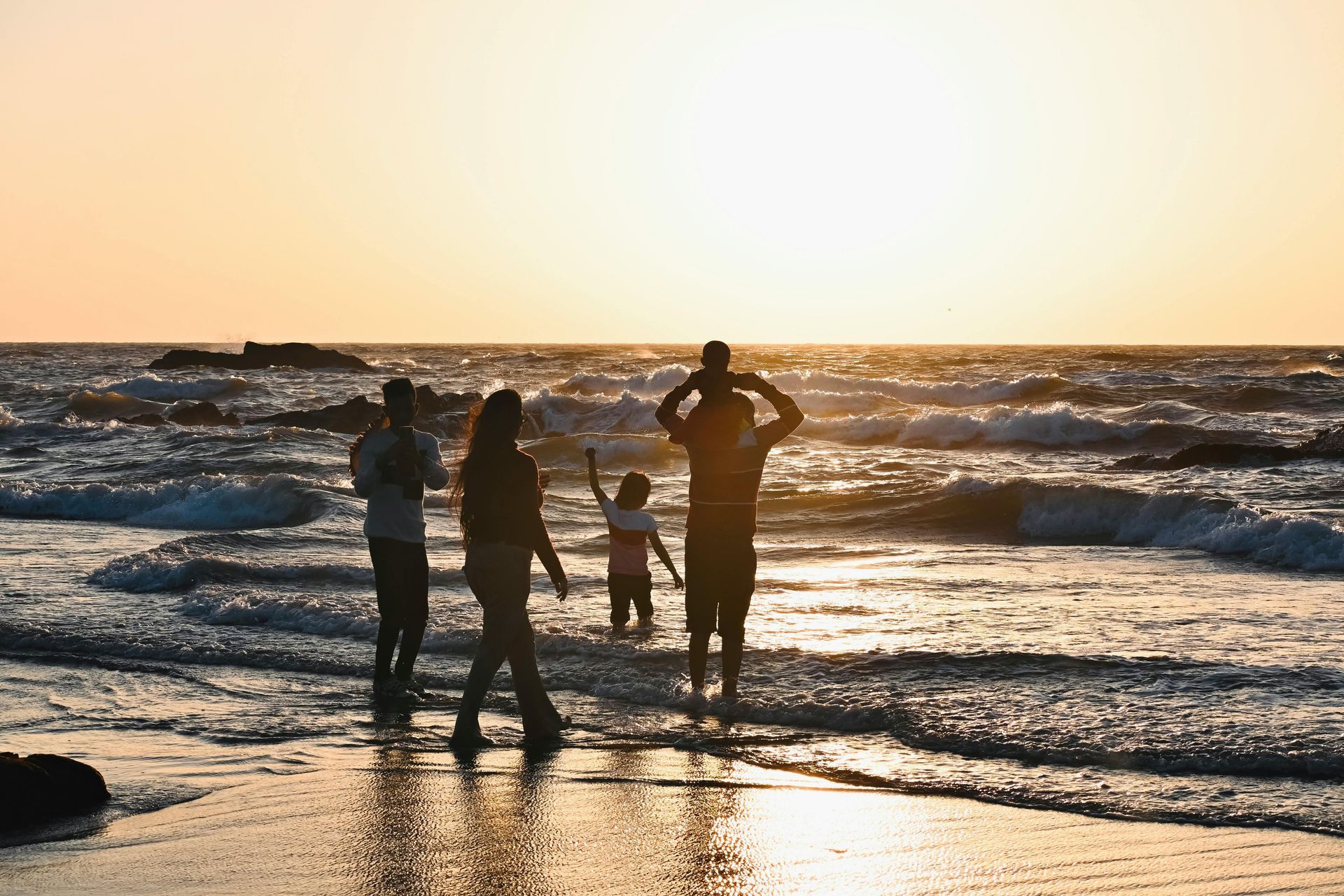People standing on a beach at sunset, watching the waves and golden light on the water.