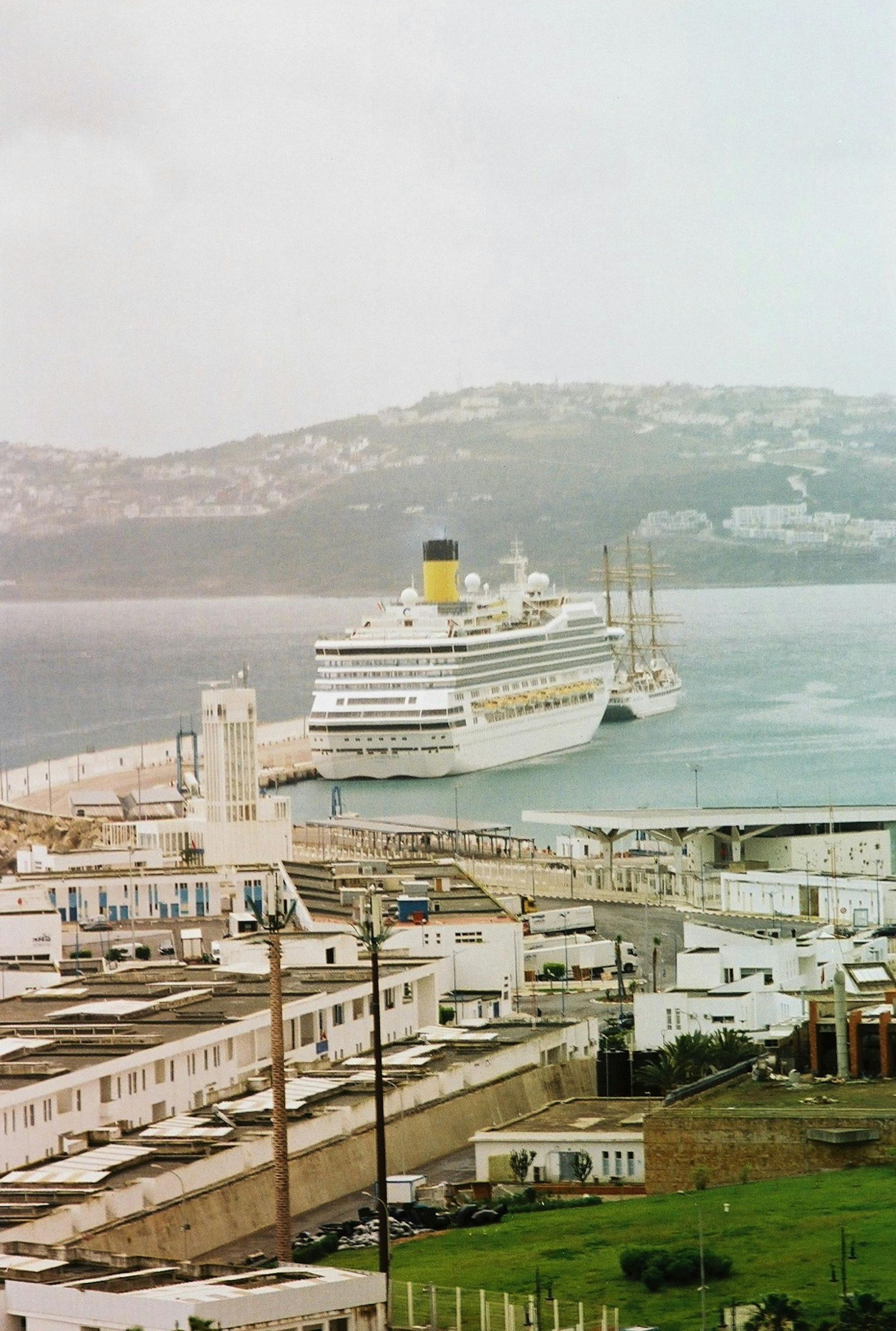 Large white cruise ship docked in a harbor with hills in the background