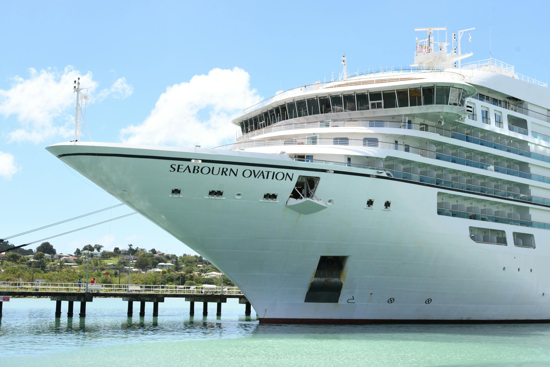 Large white cruise ship docked by a pier on calm turquoise water under a bright blue sky